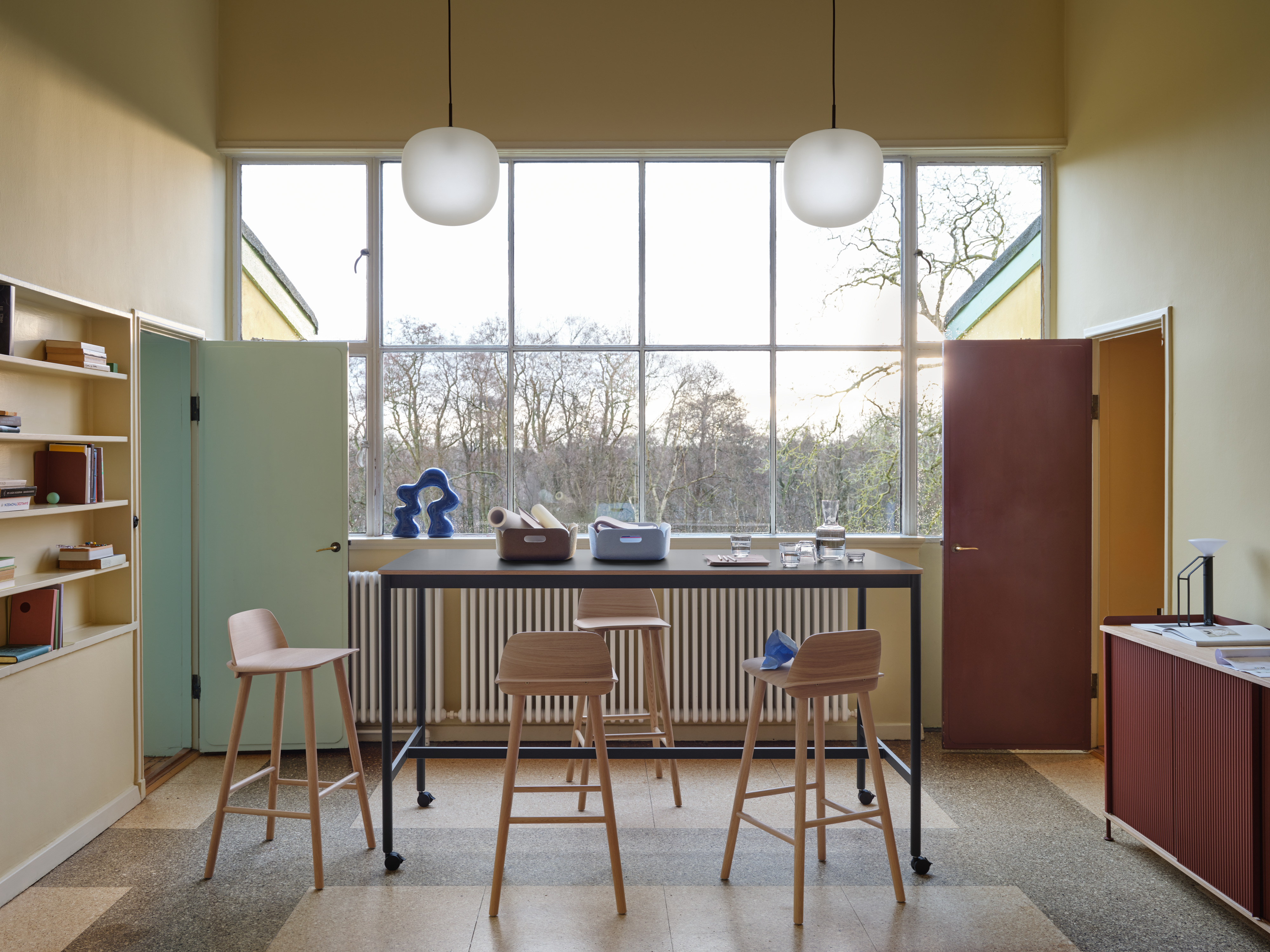 Base High Table w. Castors 190x85 cm H105 in Black - Nerd Bar Chair in Oak - Enfold Sideboard 148x45 cm H85 in Deep Red - Rime Pendant Ø37 cm in Deep Red - Restore Tray in Brown Green and Light Blue - Raise Carafe & Glasses in Clear - Piton Portable Lamp in Black - Compile Bookend in Deep Red