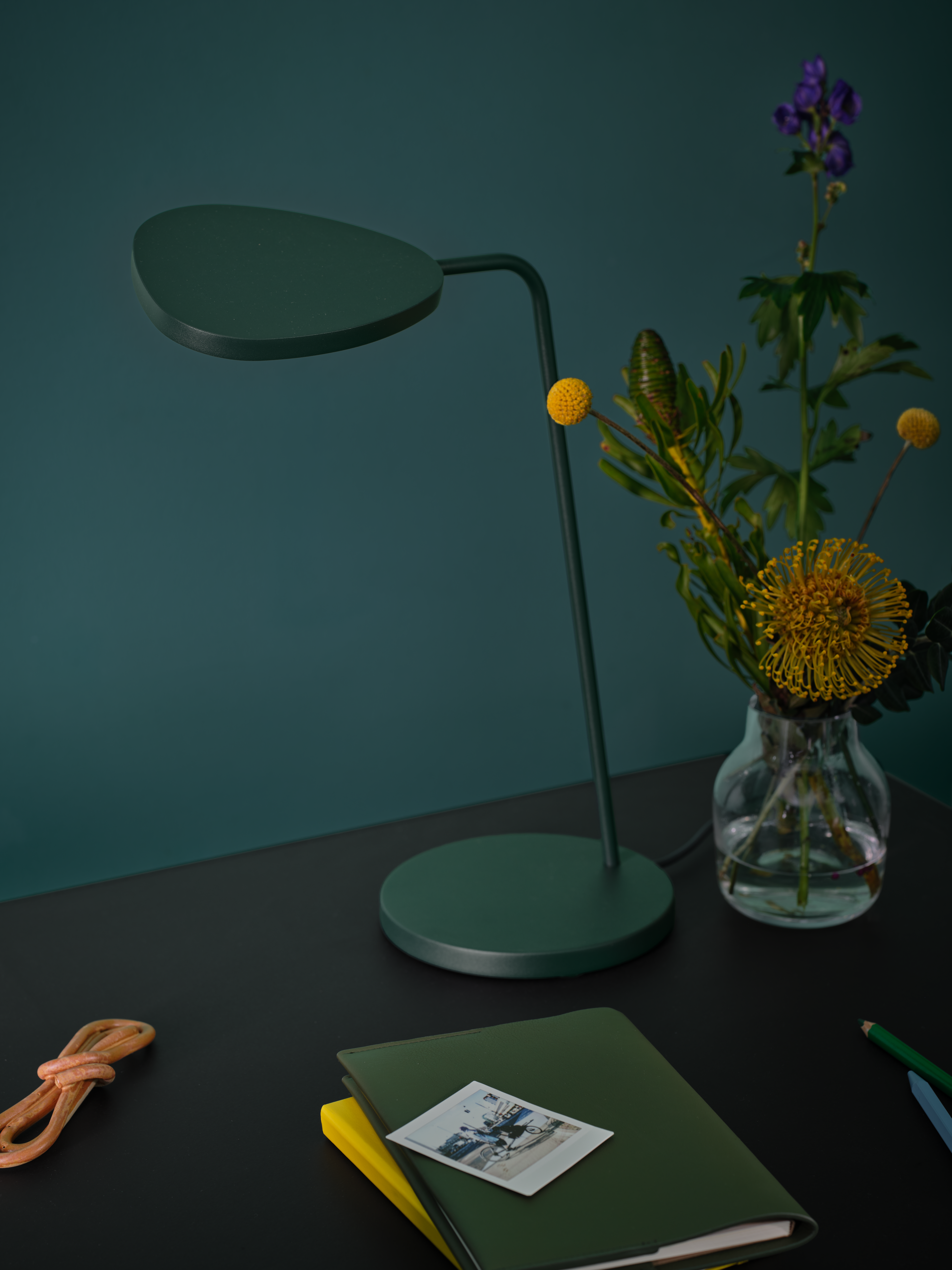 Workspace setting featuring the Leaf Table Lamp in dark green, Silent Vase 11 cm in clear glass, and the Workshop Table with black linoleum top. A minimal composition with refined, functional design.