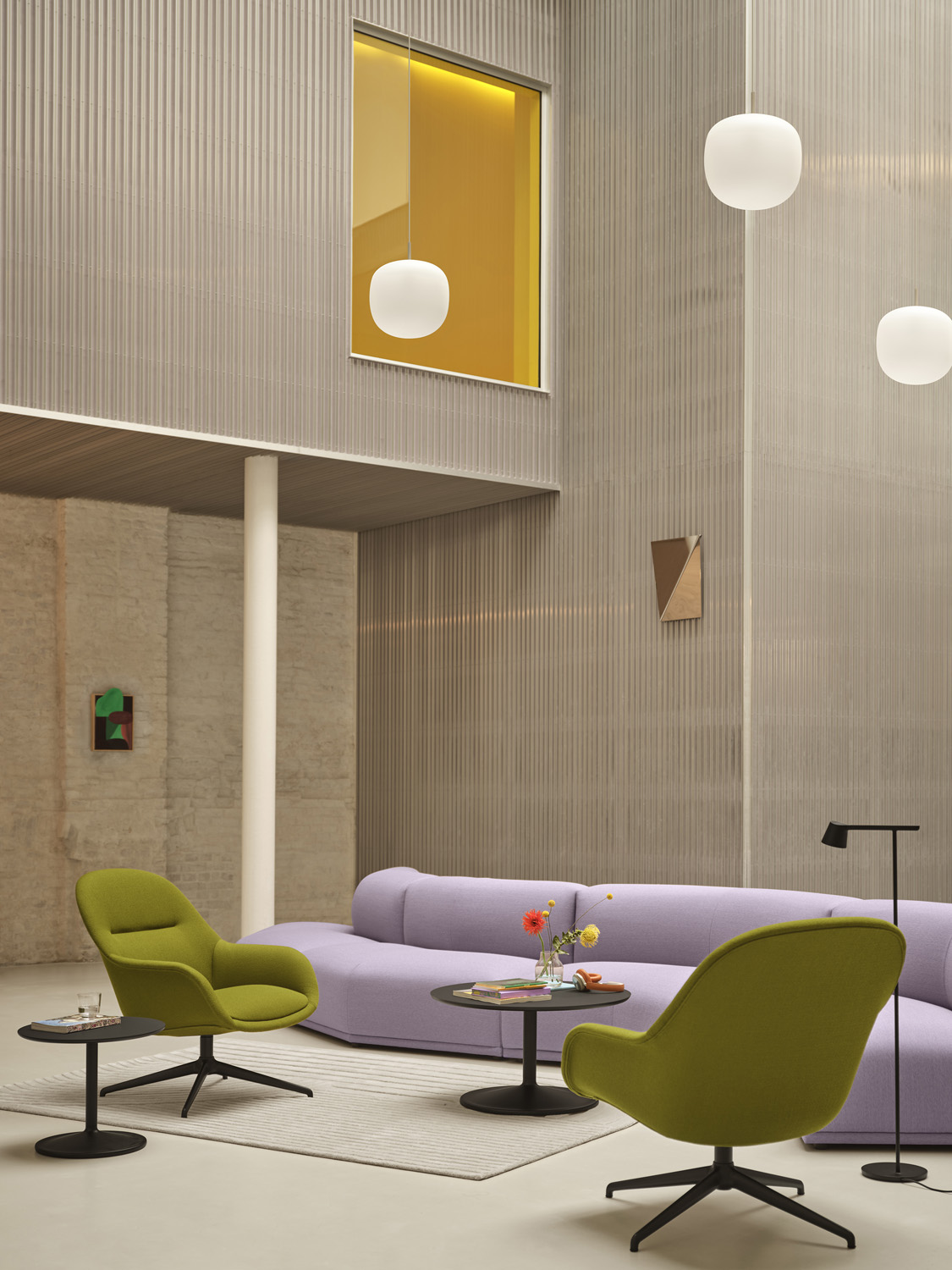 A purple sofa and two green armchairs placed in a big modern and minimalistic room together with two coffee tables in black and pendant lamps haning from the ceiling. 