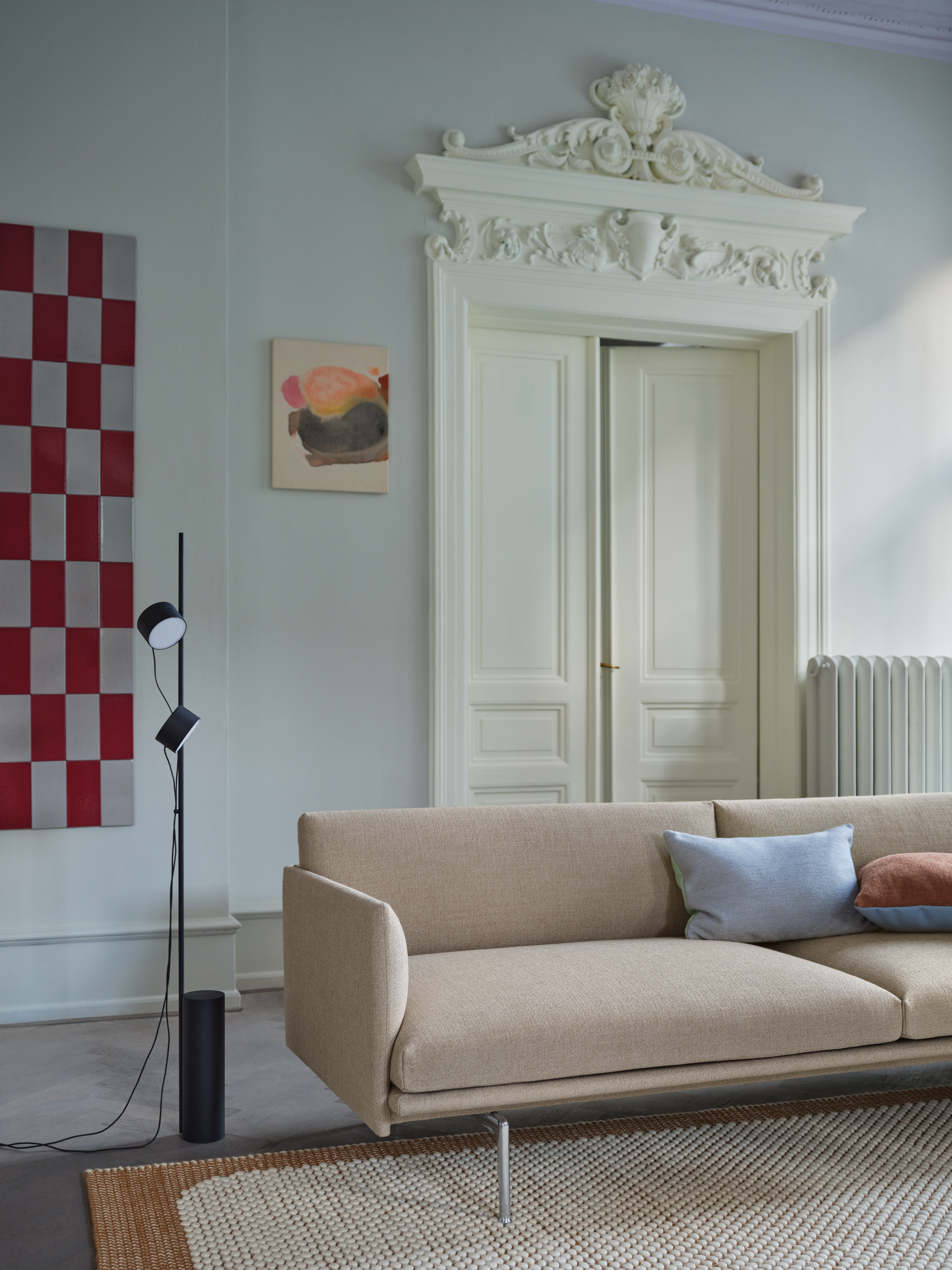 Interior setting featuring the Outline 3-Seater Sofa in Ecriture 240 with aluminium legs, Pebble Rug in burnt orange, Mingle Cushion and Post Floor Lamp.