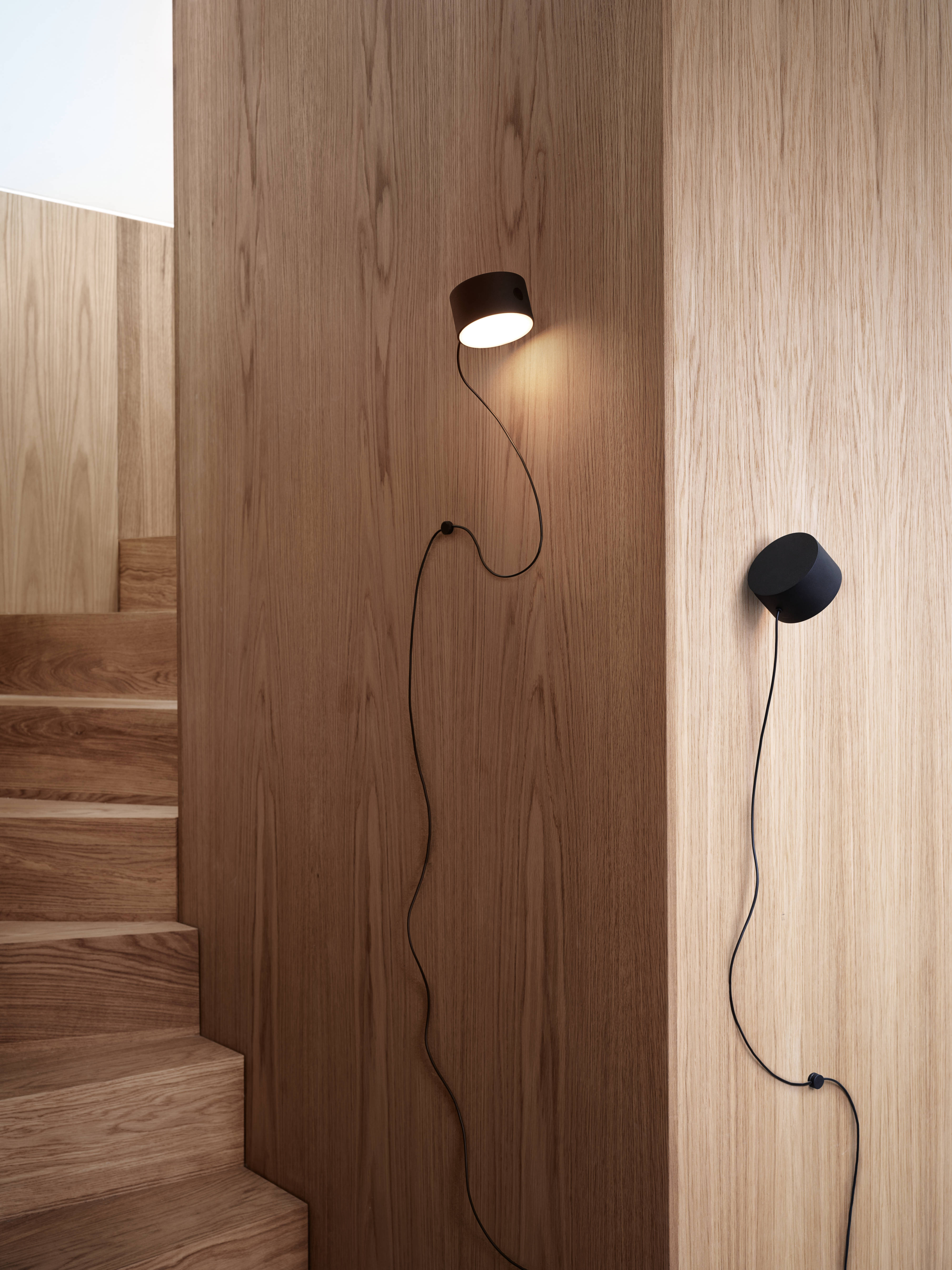 Muuto Post Wall Lamp in black, shown in a contemporary interior with a simple, functional design.