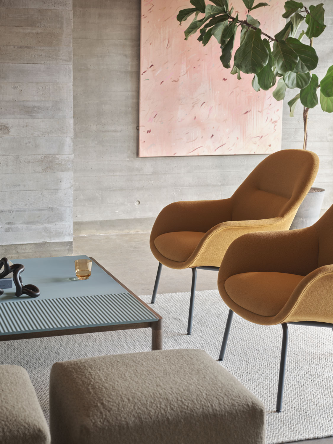 A Muuto lounge area featuring a  Fiber Lounge Armchair with a Tube Base with Grain 62016 upholstery in anthracite black. The chair is complemented by a Ply rug made from recycled polyester in off-white and an Echo pouf with Hearth 6 upholstery. The combination of textures and tones creates a modern, stylish, and inviting space.