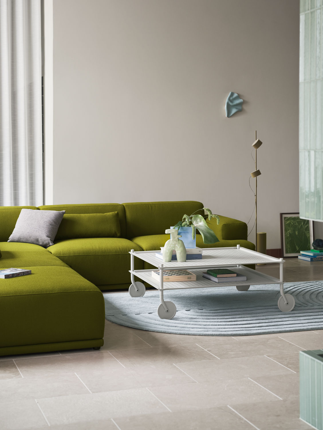 A Muuto living room featuring a grey Flow coffee table with a  Ridge vase 16 cm in light blue frosted glass. The setup includes a Connect Soft sofa with Vidar 956 upholstery and a Relevo Rug in sage green, and a Post floor lamp. The modern design and calming colors create an elegant and inviting atmosphere.