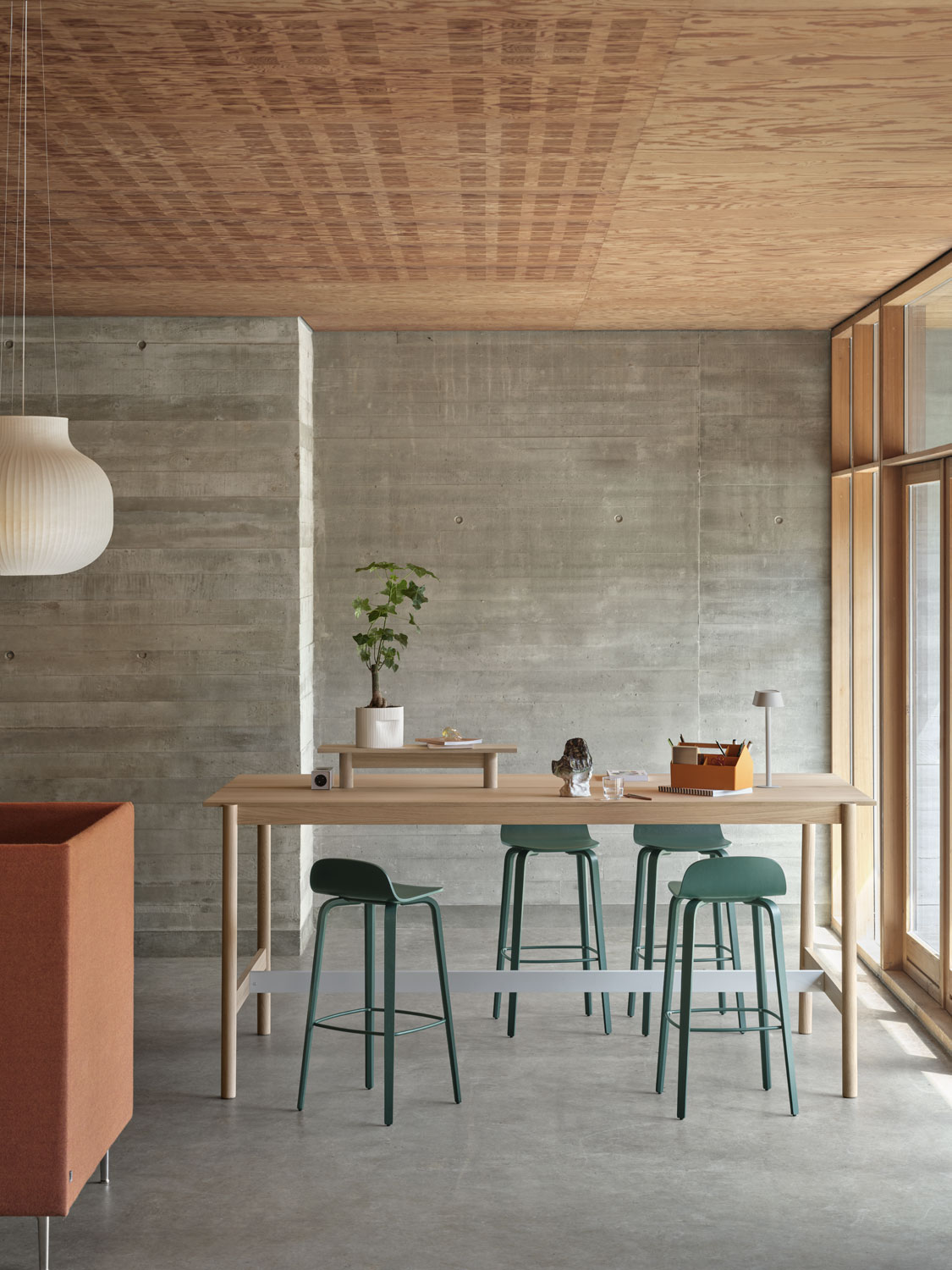 A Muuto setup featuring a Linear System high table 105 and Tray 75 cm in oak, complemented by a Visu bar stool 75 cm in dark green. The arrangement includes a Ridge planter 15 cm in off-white and a Sketch toolbox. The modern table and accessories create a refined and functional workspace.