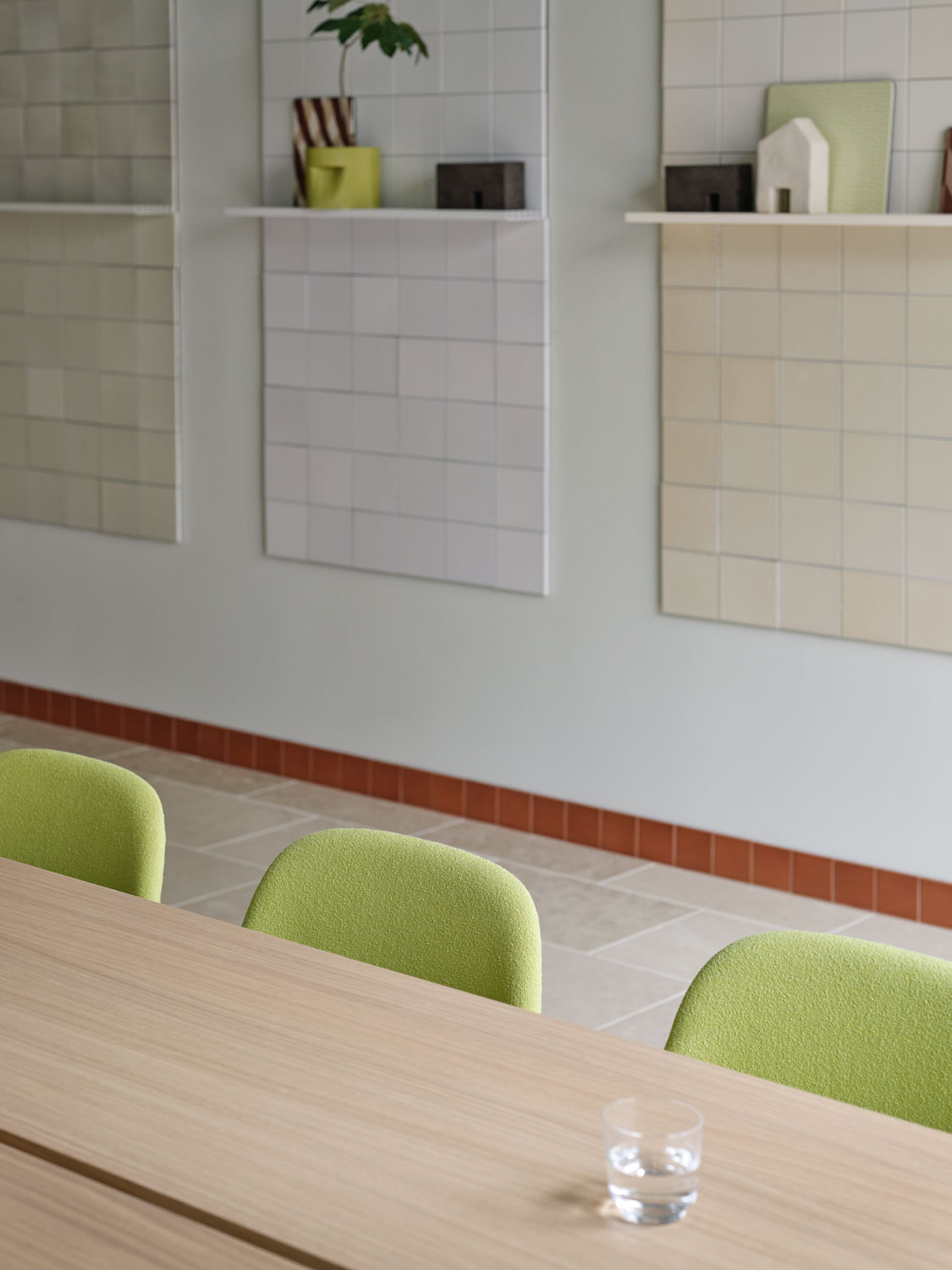 A Muuto dining setup featuring a Linear System table configuration 2 in oak, paired with a Fiber side chair with acca 961 upholstery. The scene includes Raise glasses in clear and a Ridge planter 15 cm in moss green. The combination of natural wood, modern seating, and elegant accessories creates a sophisticated and inviting dining space.
