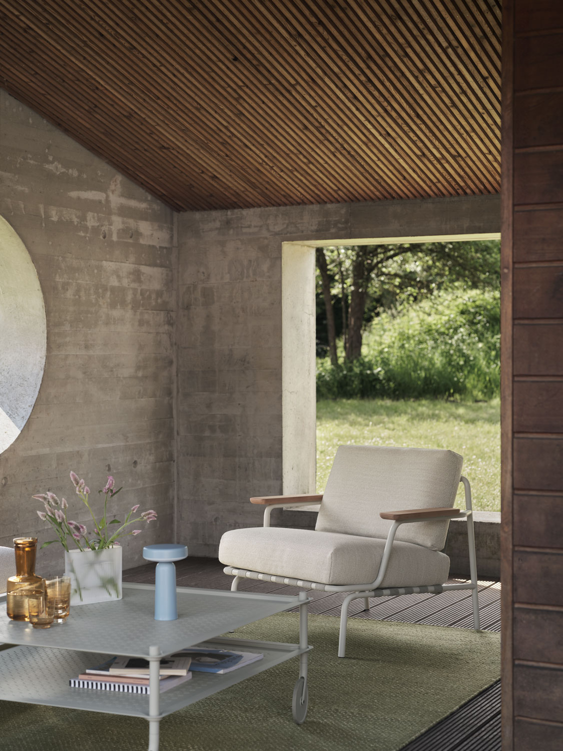 A Muuto Settle lounge chair with Laze 1 upholstery in grey paired with a Flow coffee table in grey. The setup is complemented by a moss green Ply rug made of recycled polyester and a Ridge vase in white frosted glass, creating a modern and inviting space.