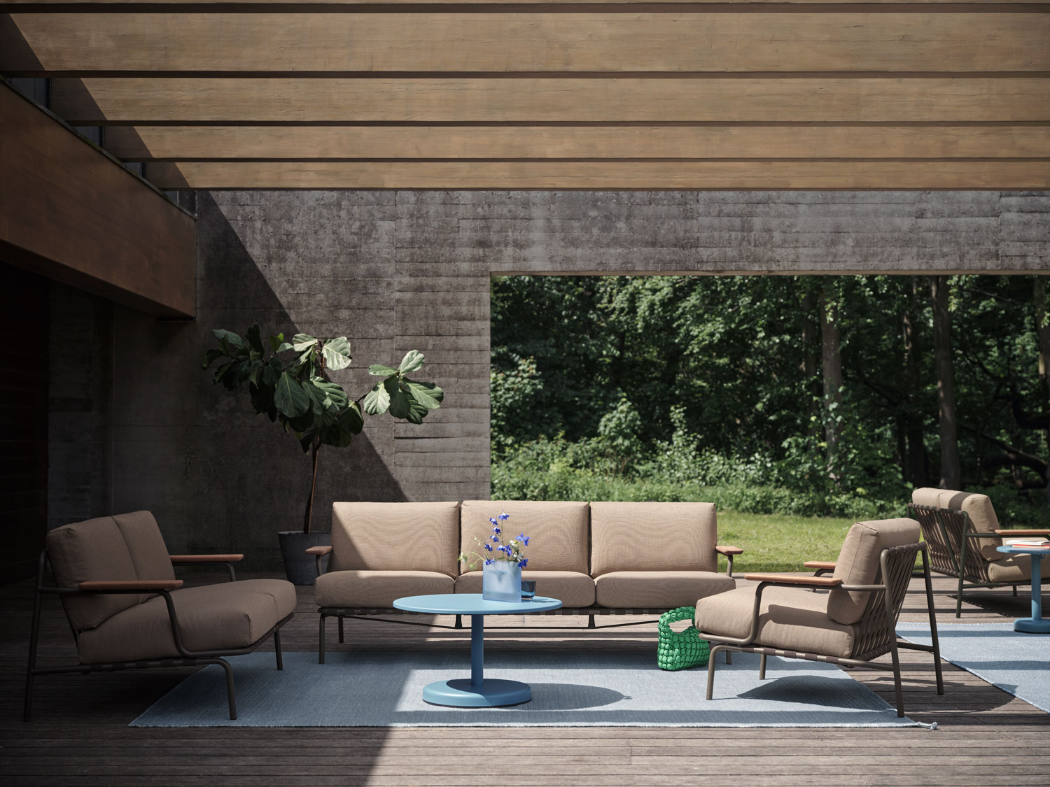 A Muuto living space featuring a Settle sofa 2 and 3 seater and lounge chair with ribbed weave upholstery in taupe. The setup includes a light blue Ply rug made from recycled polyester, a Ridge vase in glass, and a Linear steel coffee table. The blend of modern furniture and soft accents creates a stylish and inviting atmosphere.