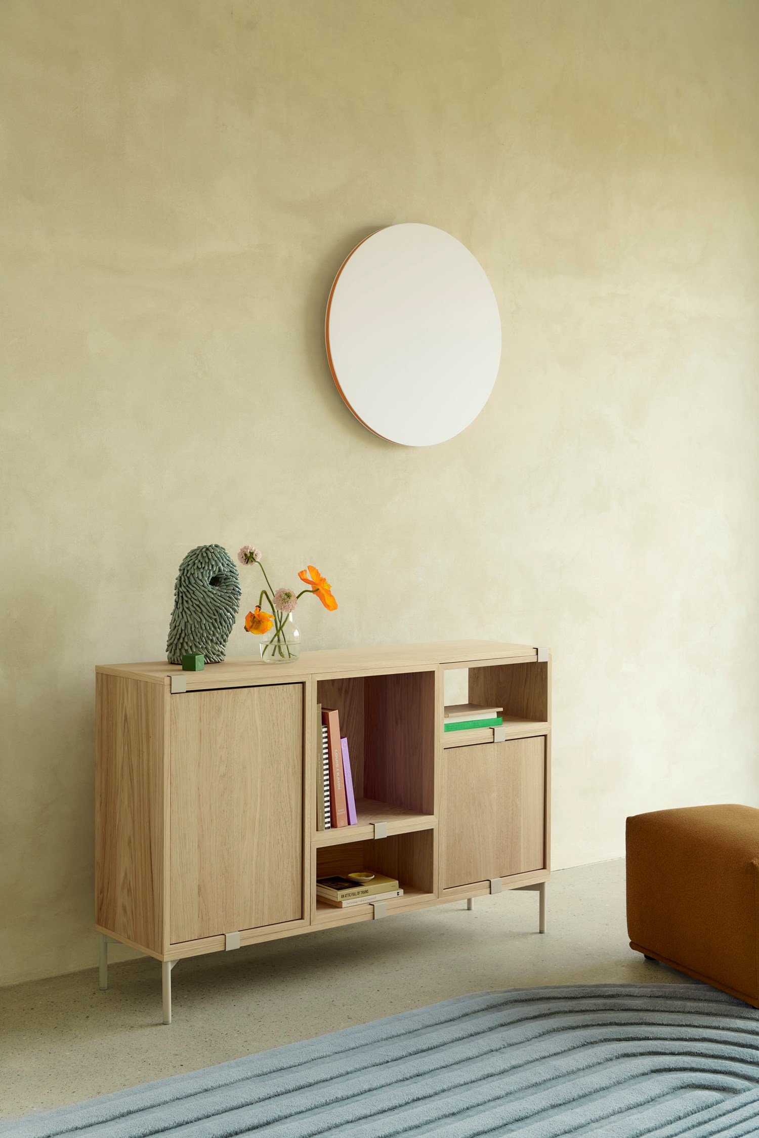 Stacked in oak is placed in a minimalistic room with brushed stone walls. A round wall lamp hangs above the storage system, casting a soft light that adds a subtle, elegant touch to the clean design. Stacked in oak is placed in a minimalistic room with brushed stone walls. A round wall lamp hangs above the storage system, casting a soft light that adds a subtle, elegant touch to the clean design.