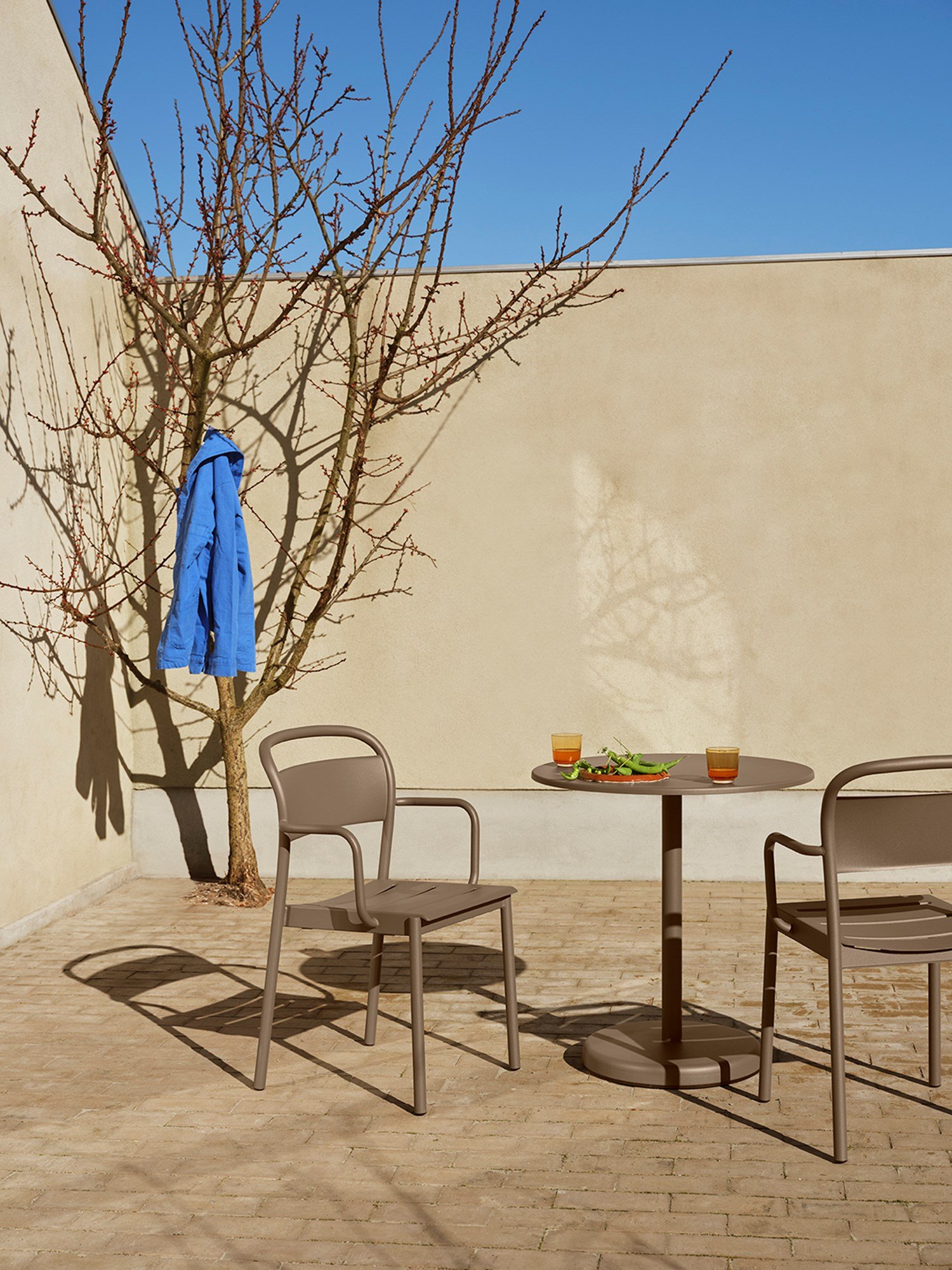 Linear steel armchairs paired with a taupe cafe table, featuring a glass top and a burnt orange Raise accessory.  Linear steel armchairs paired with a taupe cafe table, featuring a glass top and a burnt orange Raise accessory.