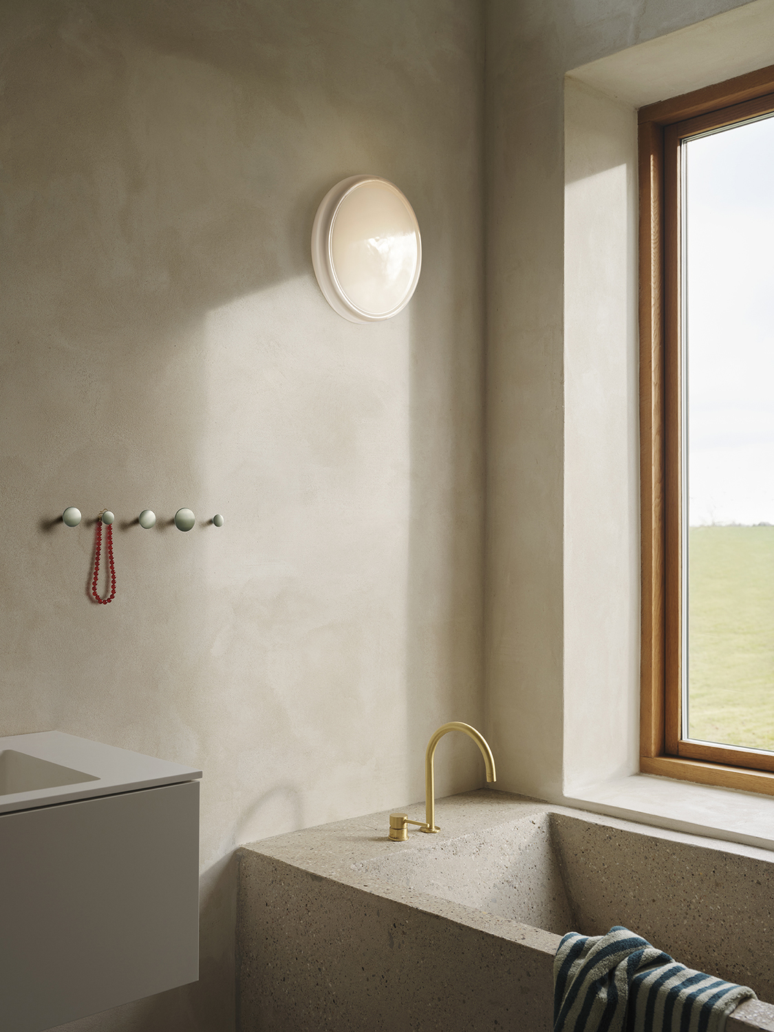 A minimalistic bathroom featuring brushed stone walls, with a round wall lamp hanging on the wall, creating a serene and modern atmosphere.