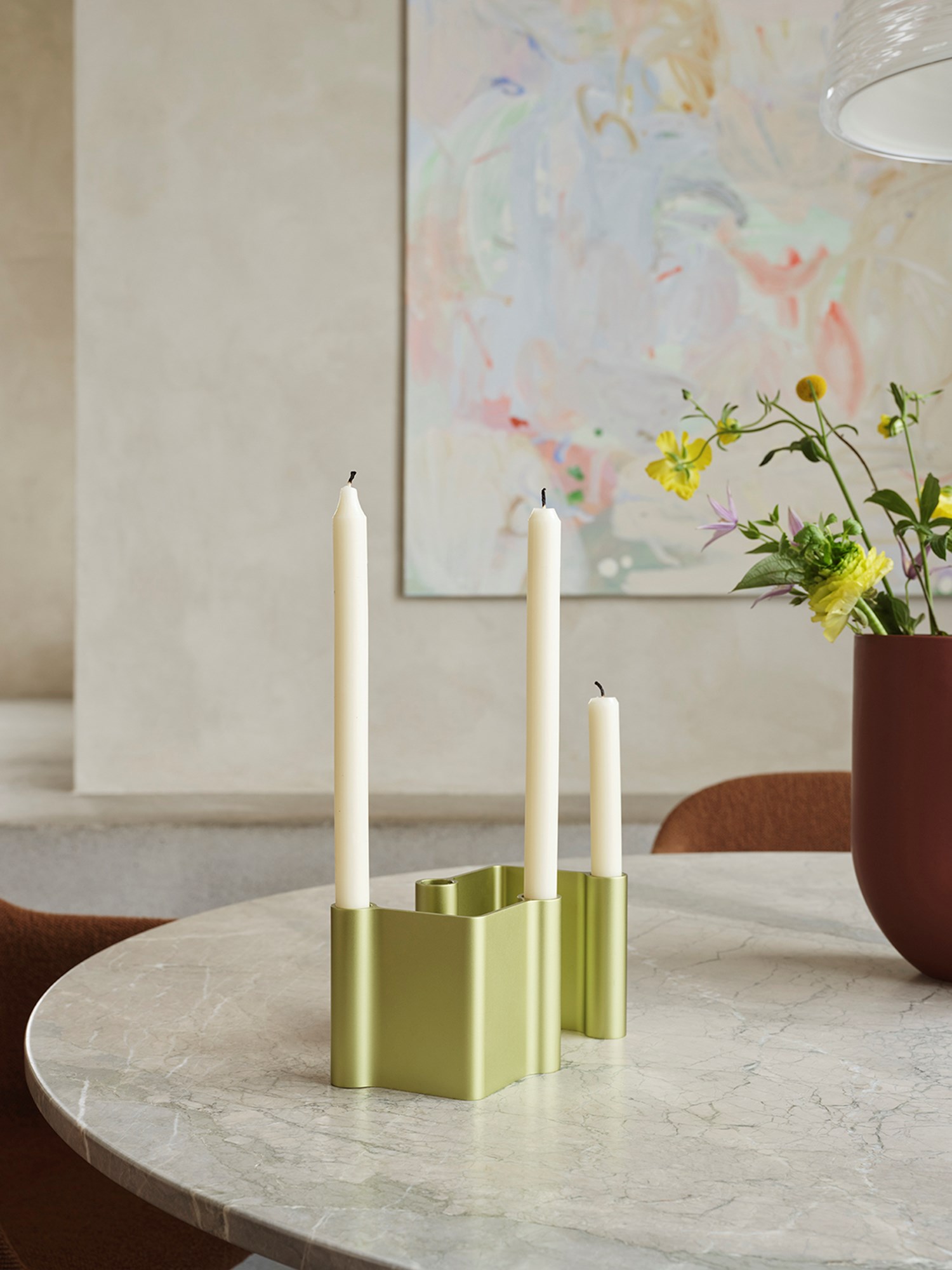 A modern candle holder in light green metal sits on a marble table, styled alongside a sculptural vase in a deep burgundy color for a striking, contemporary look. A modern candle holder in light green metal sits on a marble table, styled alongside a sculptural vase in a deep burgundy color for a striking, contemporary look.