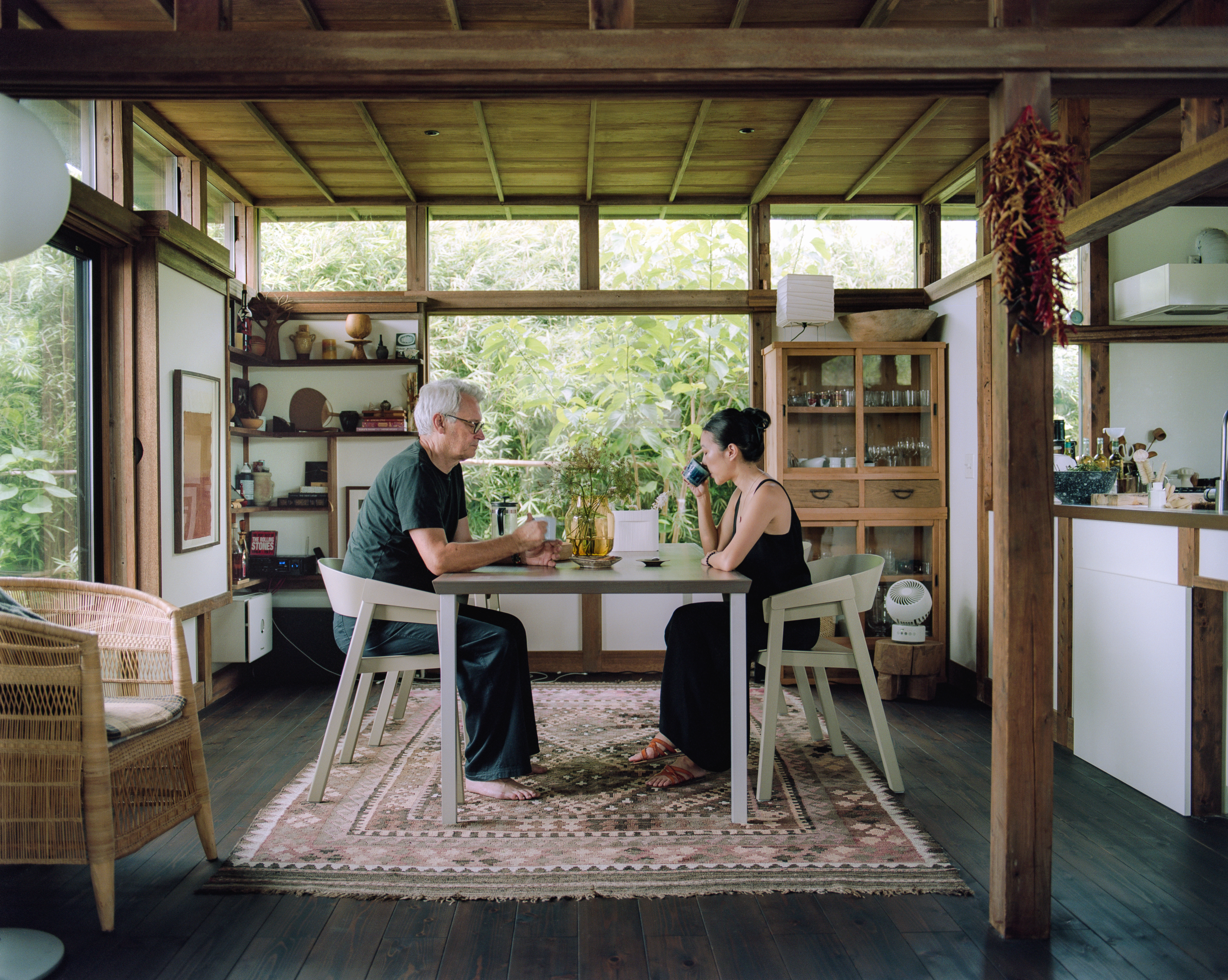 Giselle and Philippe at a dining table in a bright, wood-paneled room sitting on Cover Armchairs. 