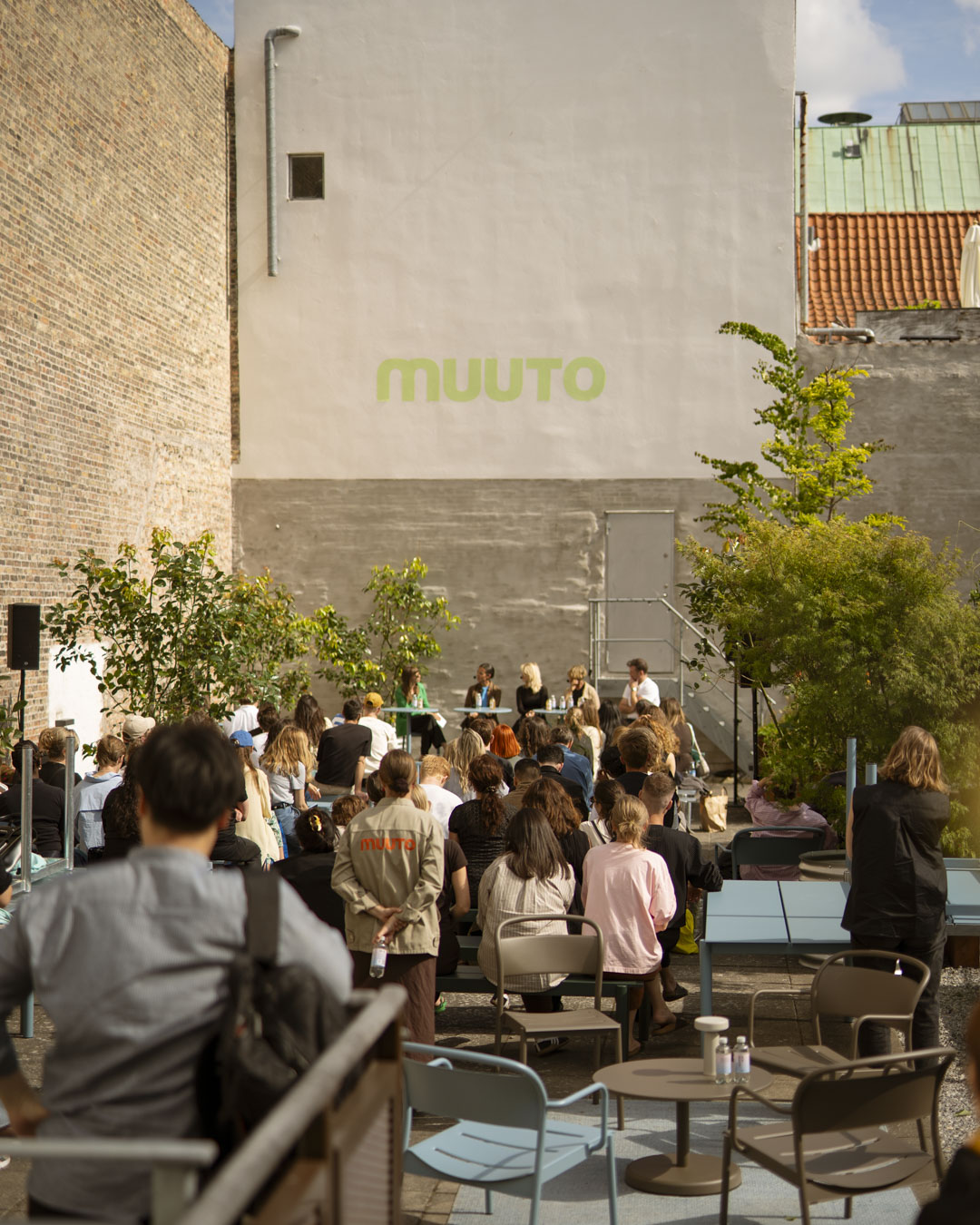 Audience gathered in a sunlit courtyard during Muuto’s panel talk, seated on modern Muuto furniture in a thoughtfully designed outdoor setting.