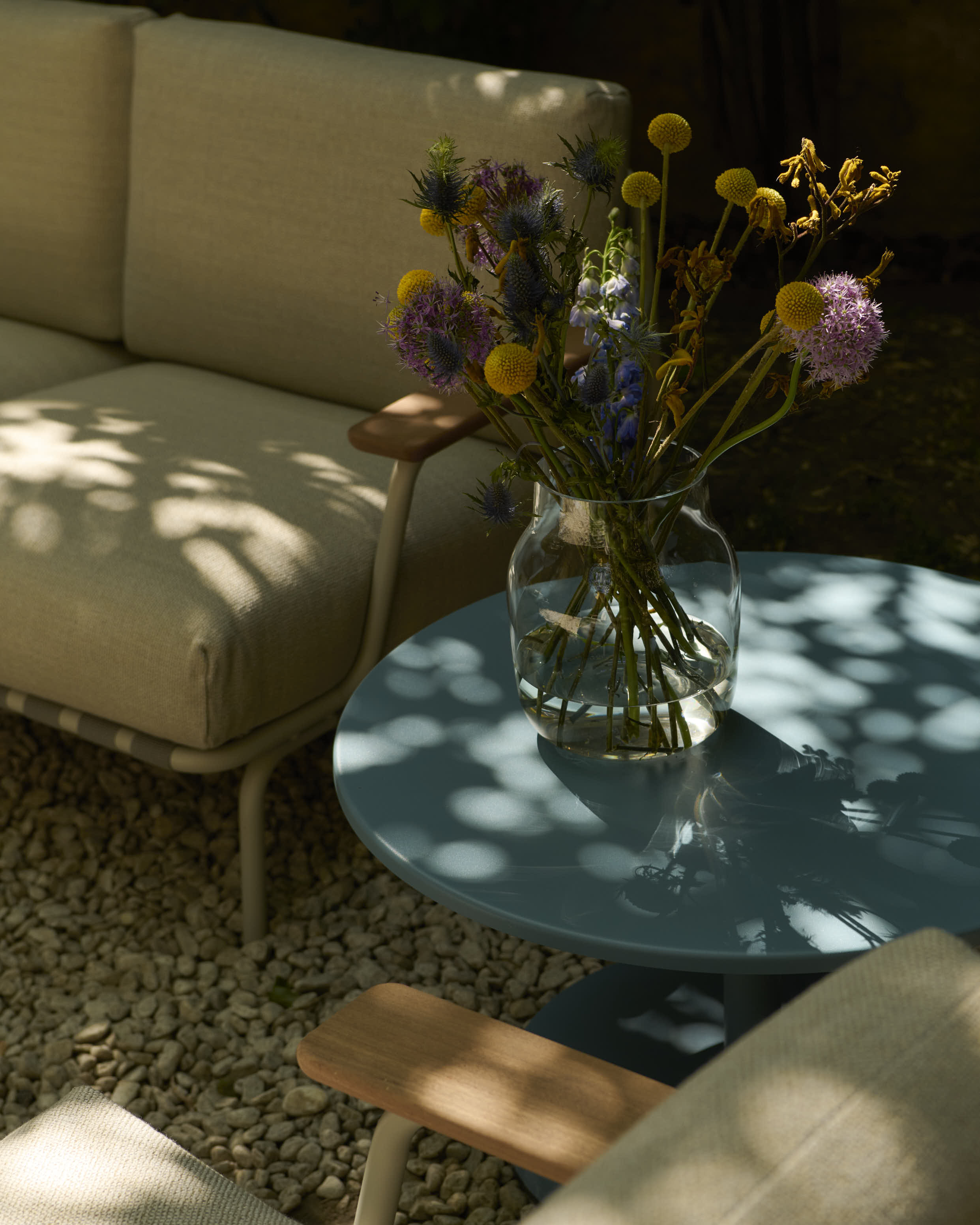 A close-up of a clear vase with colorful flowers placed on a light blue outdoor coffee table. 