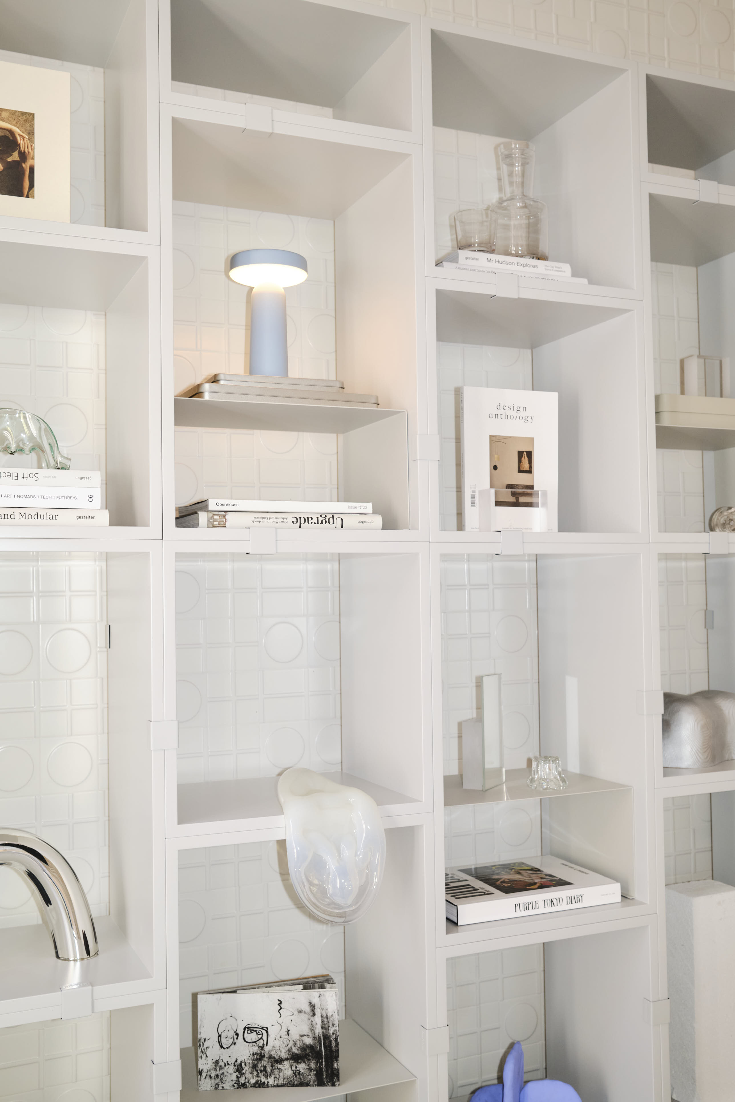 A close-up of a white bookcase styled with a table lamp, books, and decorative design objects.