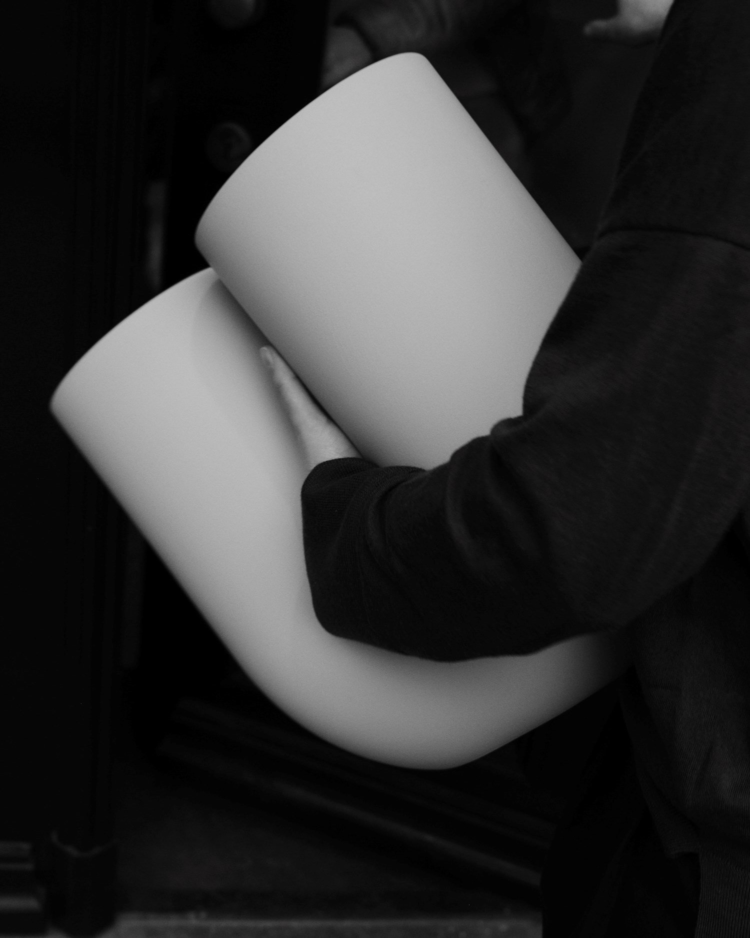 In a black-and-white close-up, Rachel holds a Kink Vase close to their torso. 
 In a black-and-white close-up, Rachel holds a Kink Vase close to their torso.