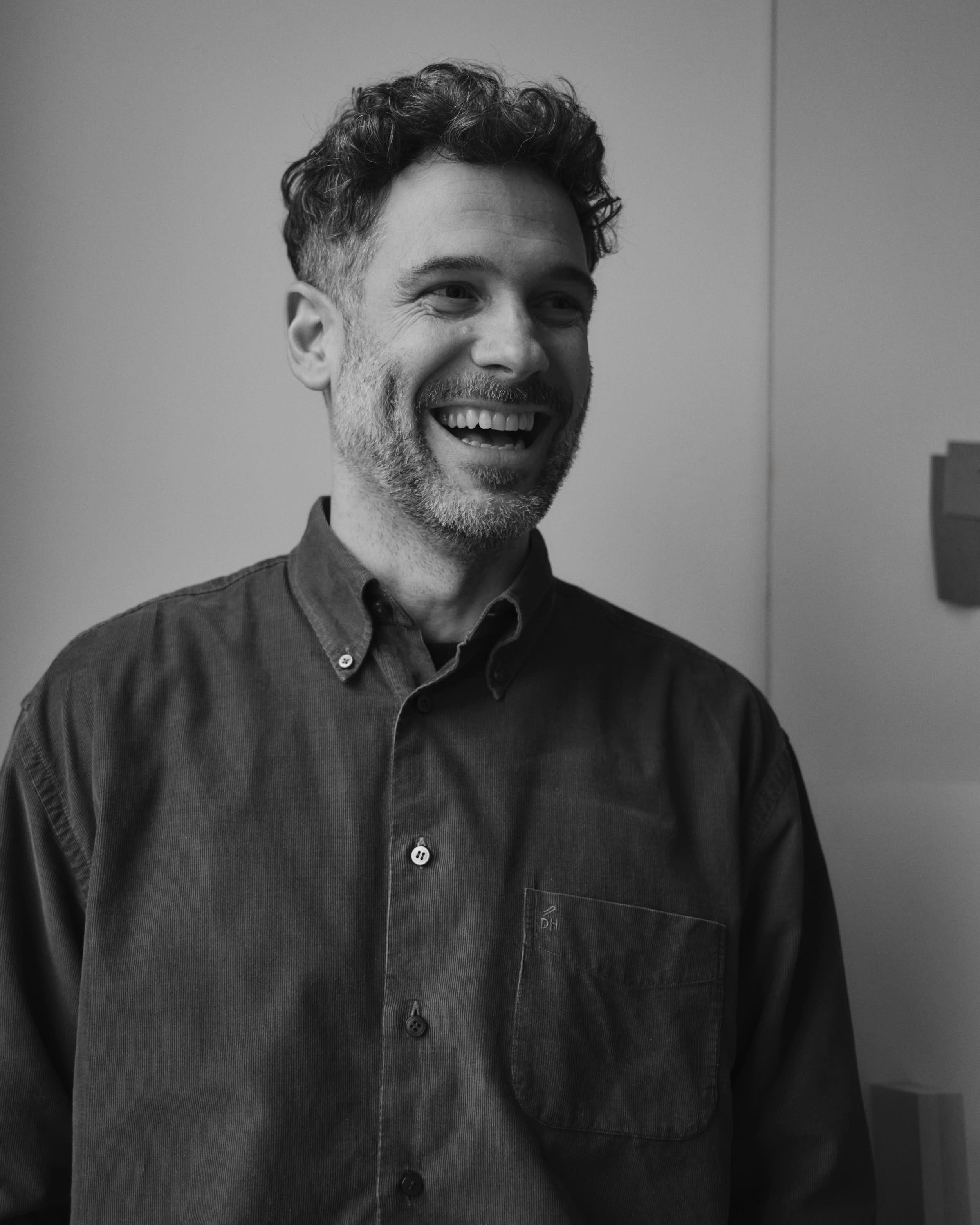 A black-and-white portrait of Johan smiling wearing a dark button-up shirt, captured in a candid moment.
