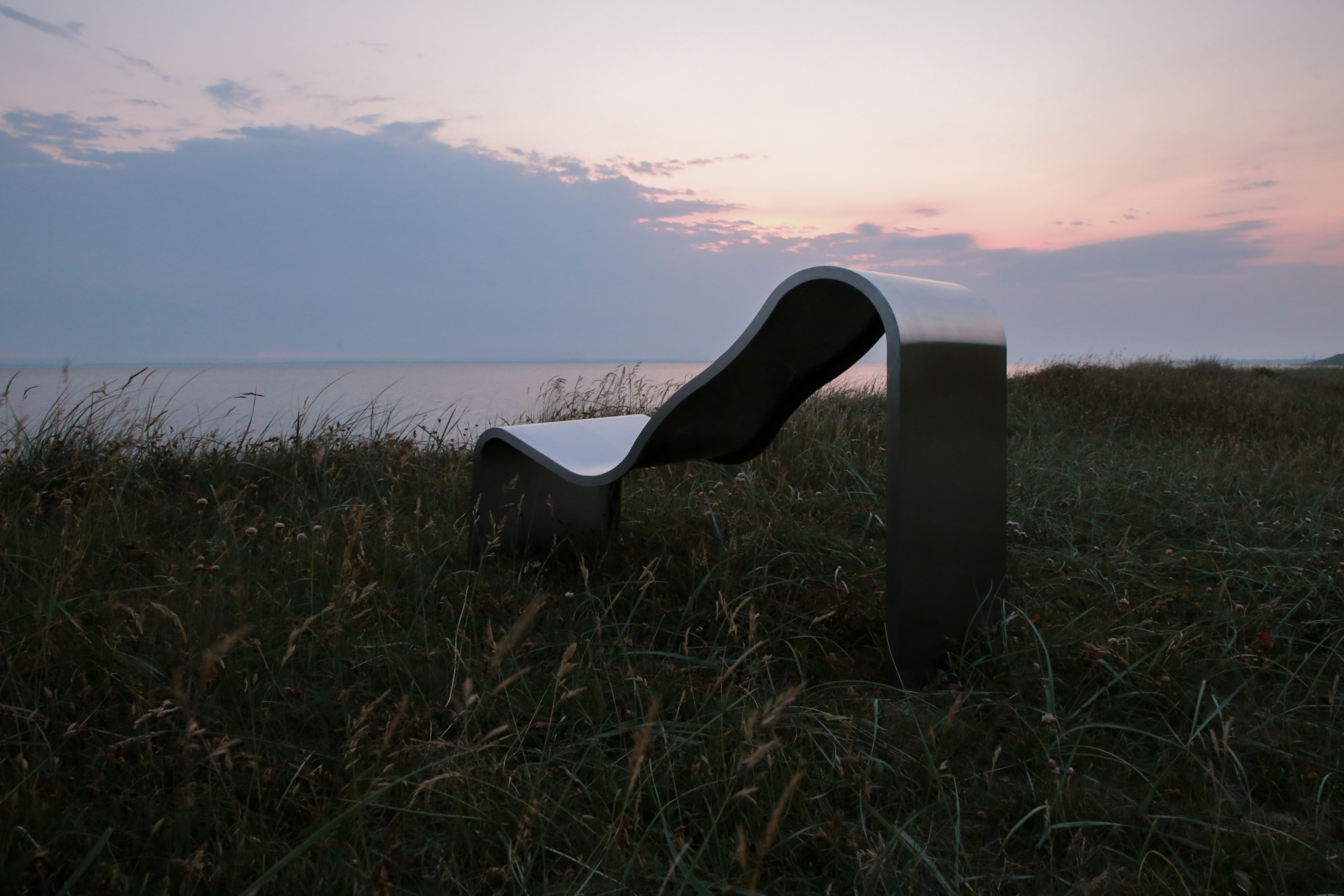 The Dream View Chair is placed outdoors on a green grass field, bathed in the warm glow of the sunset.