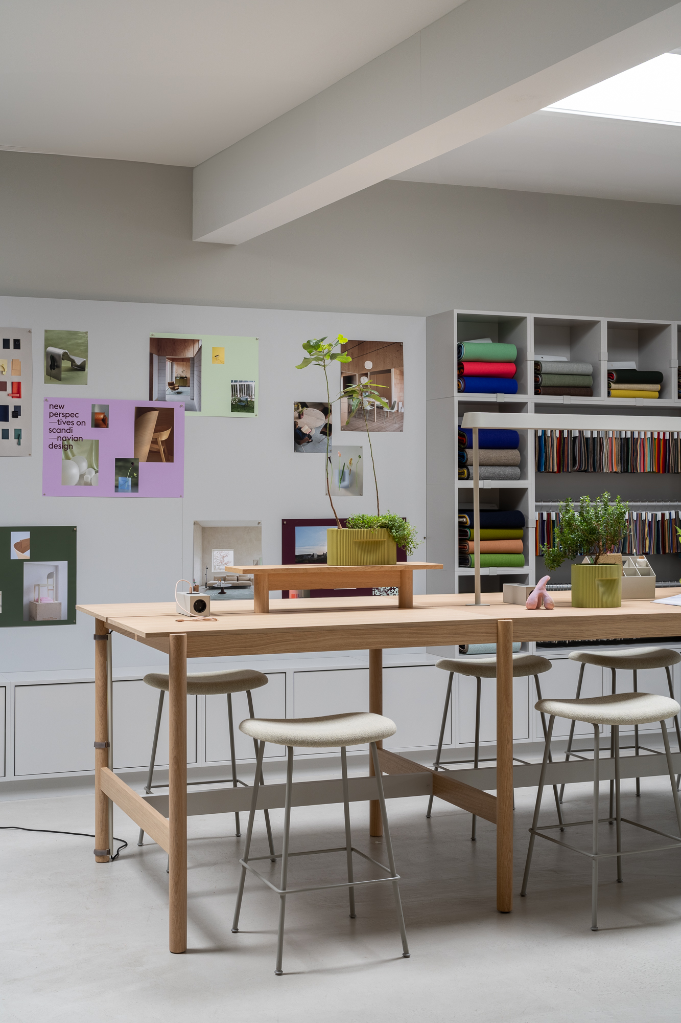 A Linear High System Table is placed in a creative space surrounded by minimalistic chairs.  Green plants are placed on the table creating a comfy atmosphere.