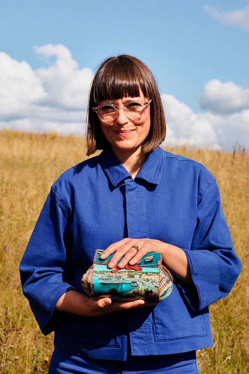 Stine Find Osther Vice President of Design at Kvadrat wearing a blue shirt, holding textiles in a wheat field. 