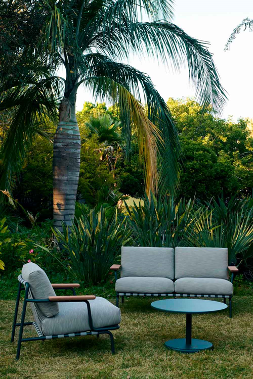 An outdoor setting with two sofas and a blue coffee table placed on grass between palm trees