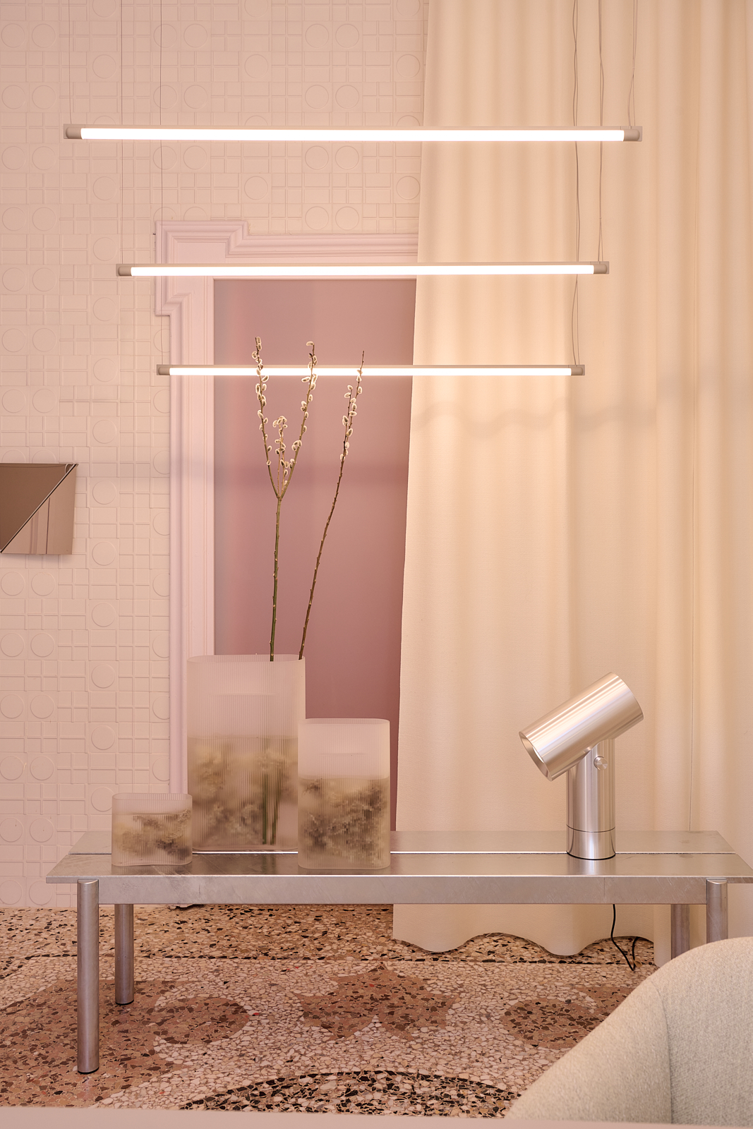 Image of Muuto's Milan Apartment. A ligtht dusty rose room where a metal bench is placed styled together with a metal table lamp and glass vases. 