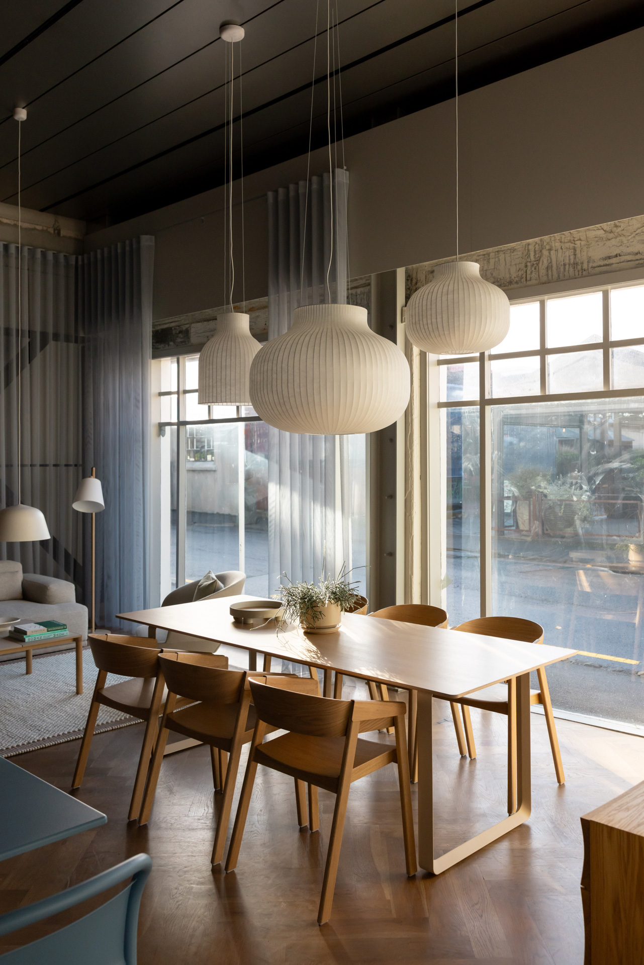 A dining setting featuring a wooden dining table with matching wooden chairs. White pendant lamps hang above, creating a cozy atmosphere.