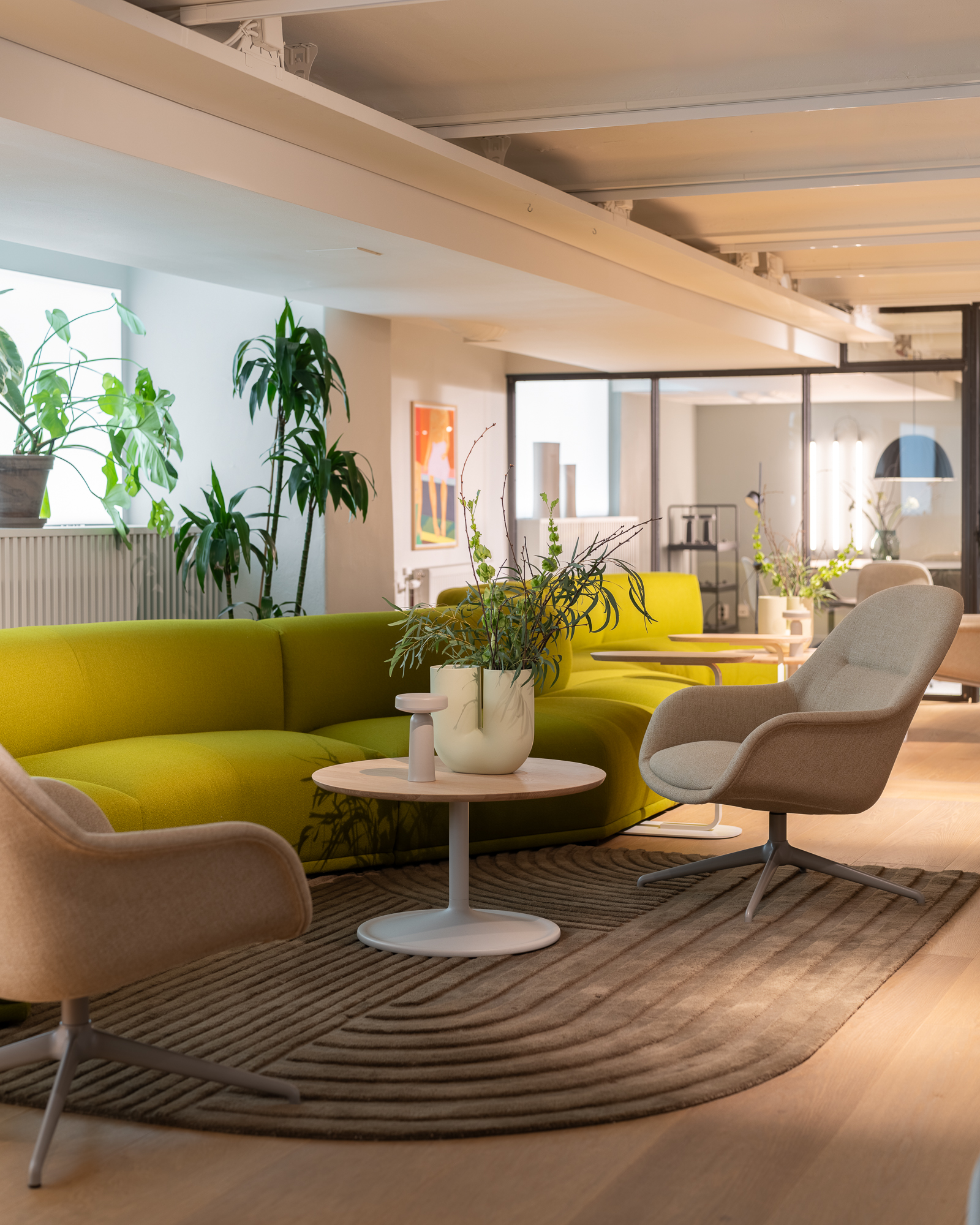 Bright and stylish lounge area at Muuto's Stockholm store. Vibrant green sofa, elegant chairs, and lush plants enhance the contemporary interior design.